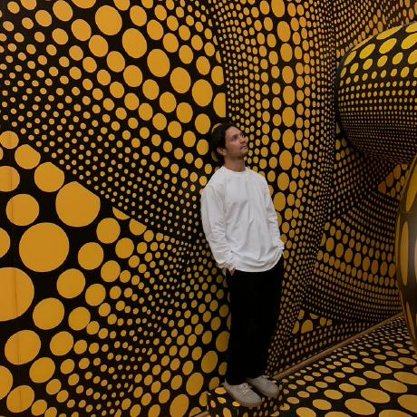 Ronny Glotzbach, stehend vor einer gepunkteten Wandinstallation in Gelb und Schwarz.